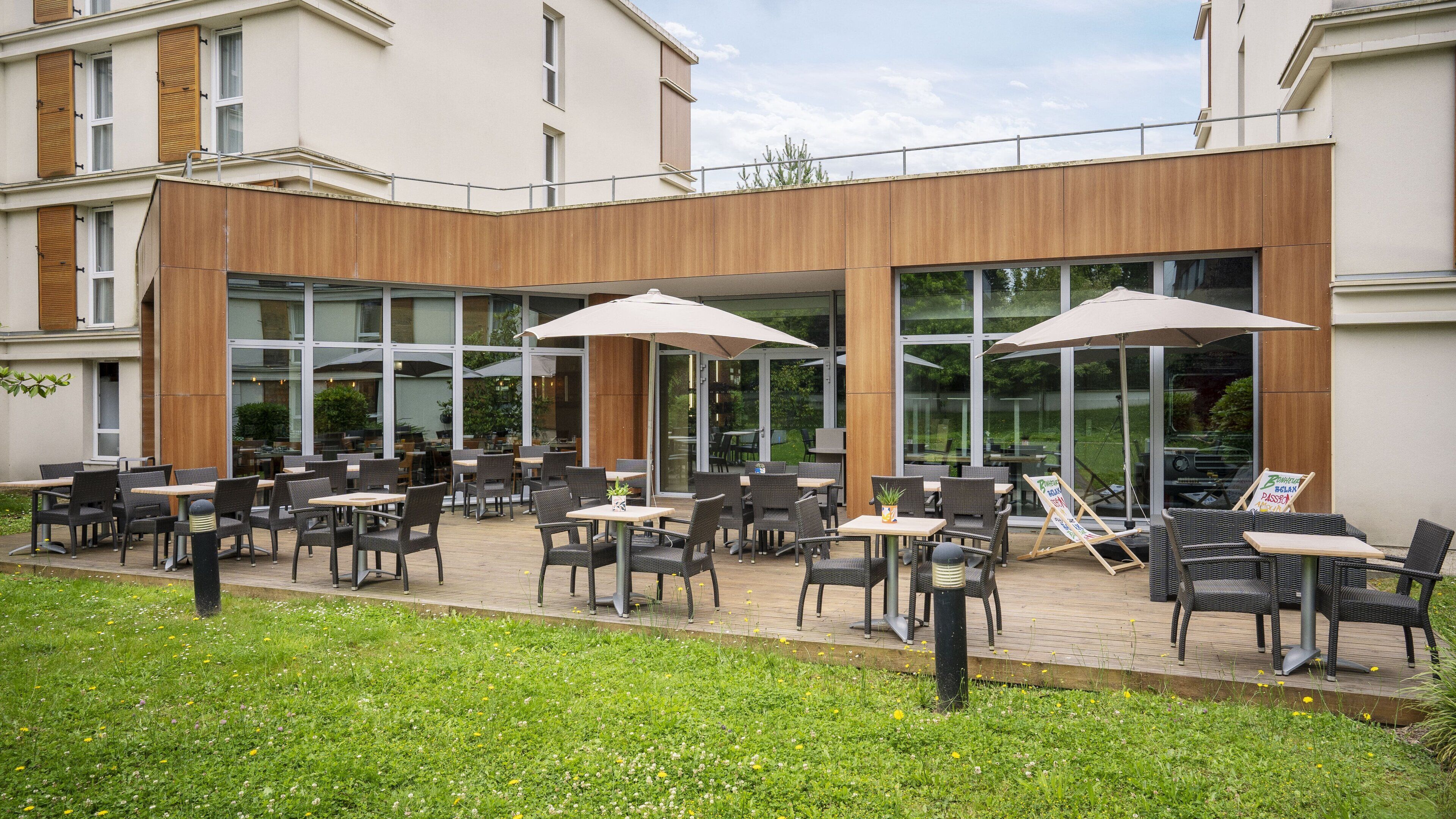 An outdoor patio area with tables and chairs, large umbrellas, and a wooden facade.