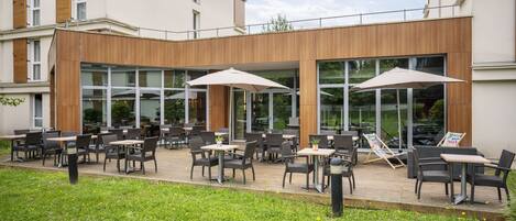 An outdoor patio area with tables and chairs, large umbrellas, and a wooden facade.
