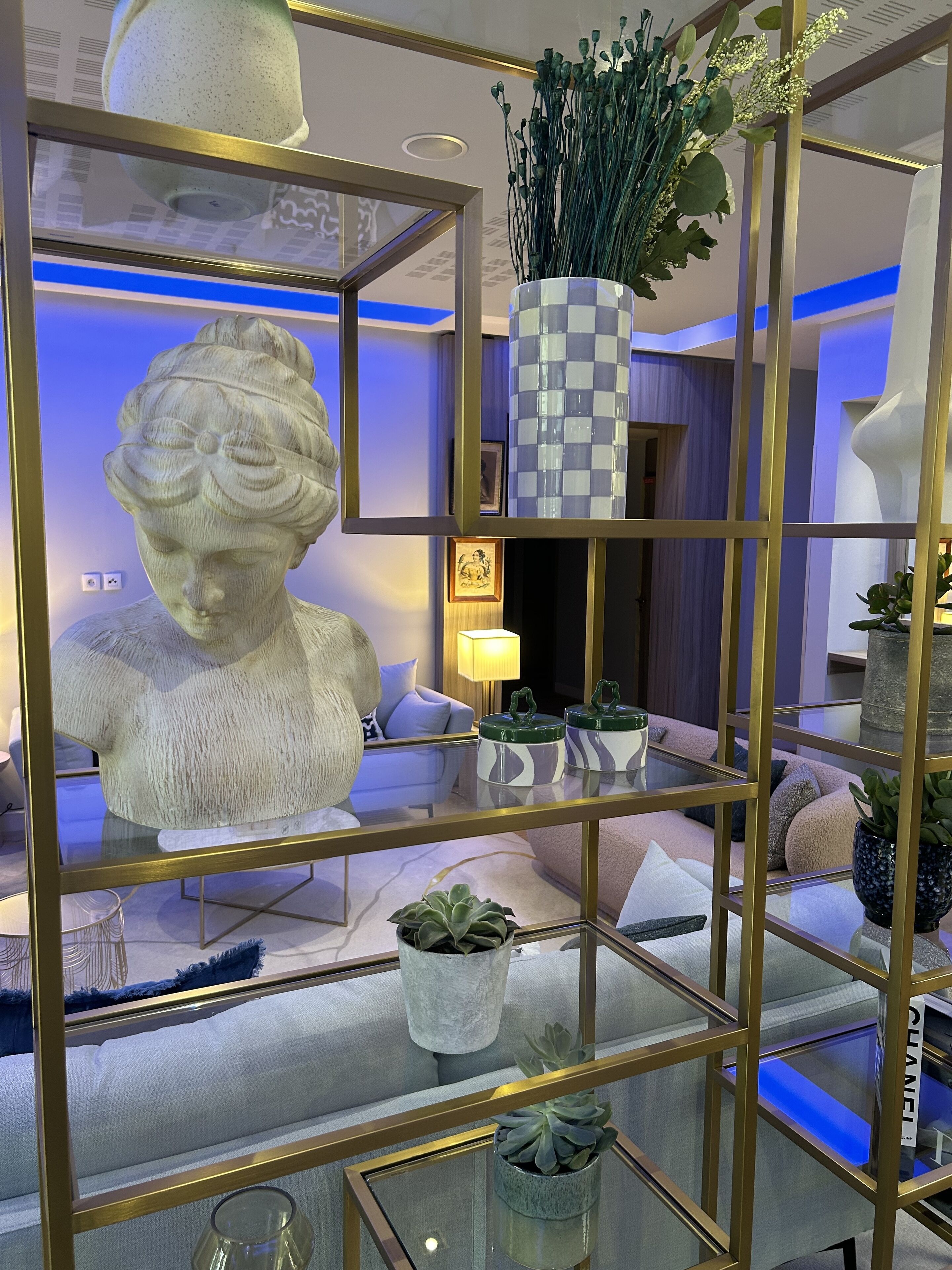 Ein modernes Wohnzimmer mit einer Glastausche, in der eine Büstenstatue, dekorative Vasen und Topfpflanzen ausgestellt sind.