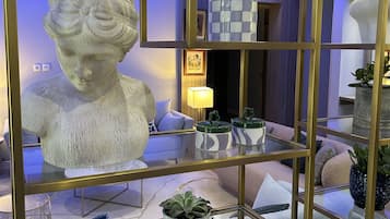 A modern living room with a glass display case containing a bust sculpture, decorative vases, and potted plants.