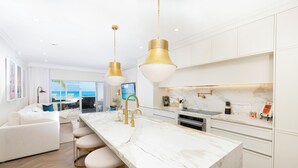 A modern kitchen with a marble countertop, gold fixtures, and a large island with bar stools. - The Grandview Condos on Seven Mile Beach (Seven Mile Beach)