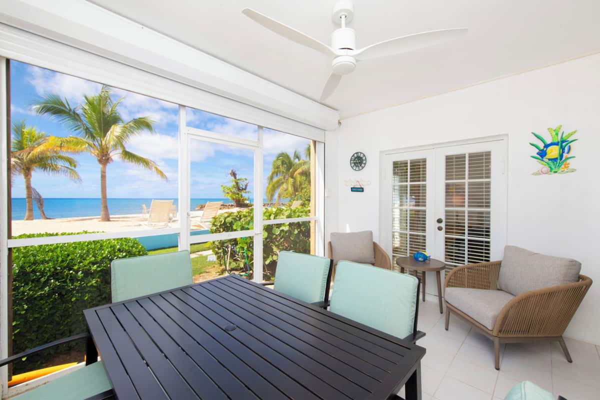 A sunlit room with a view of the beach, a ceiling fan, and a dining table with chairs.