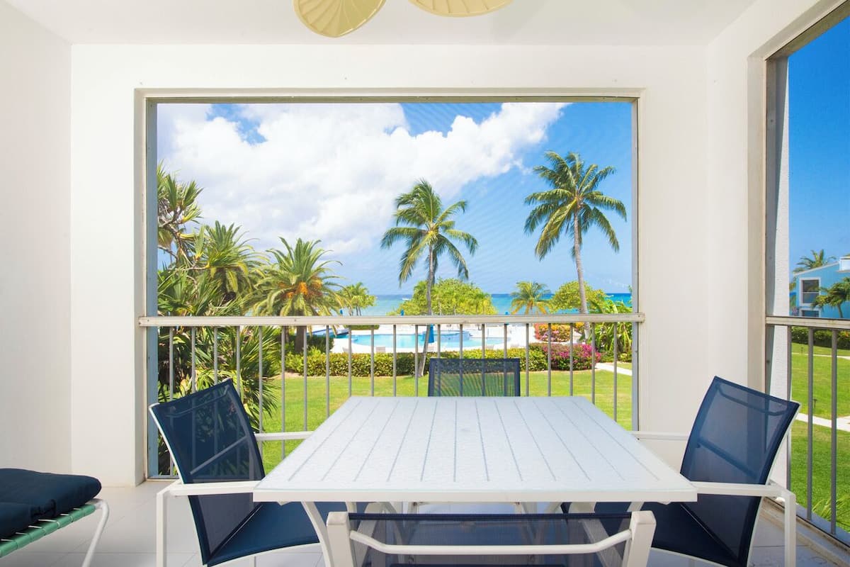 A balcony with a white table and chairs, overlooking a pool and palm trees.