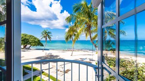 A balcony with a view of a beach, palm trees, and the ocean. - The Grandview Condos on Seven Mile Beach (Seven Mile Beach)