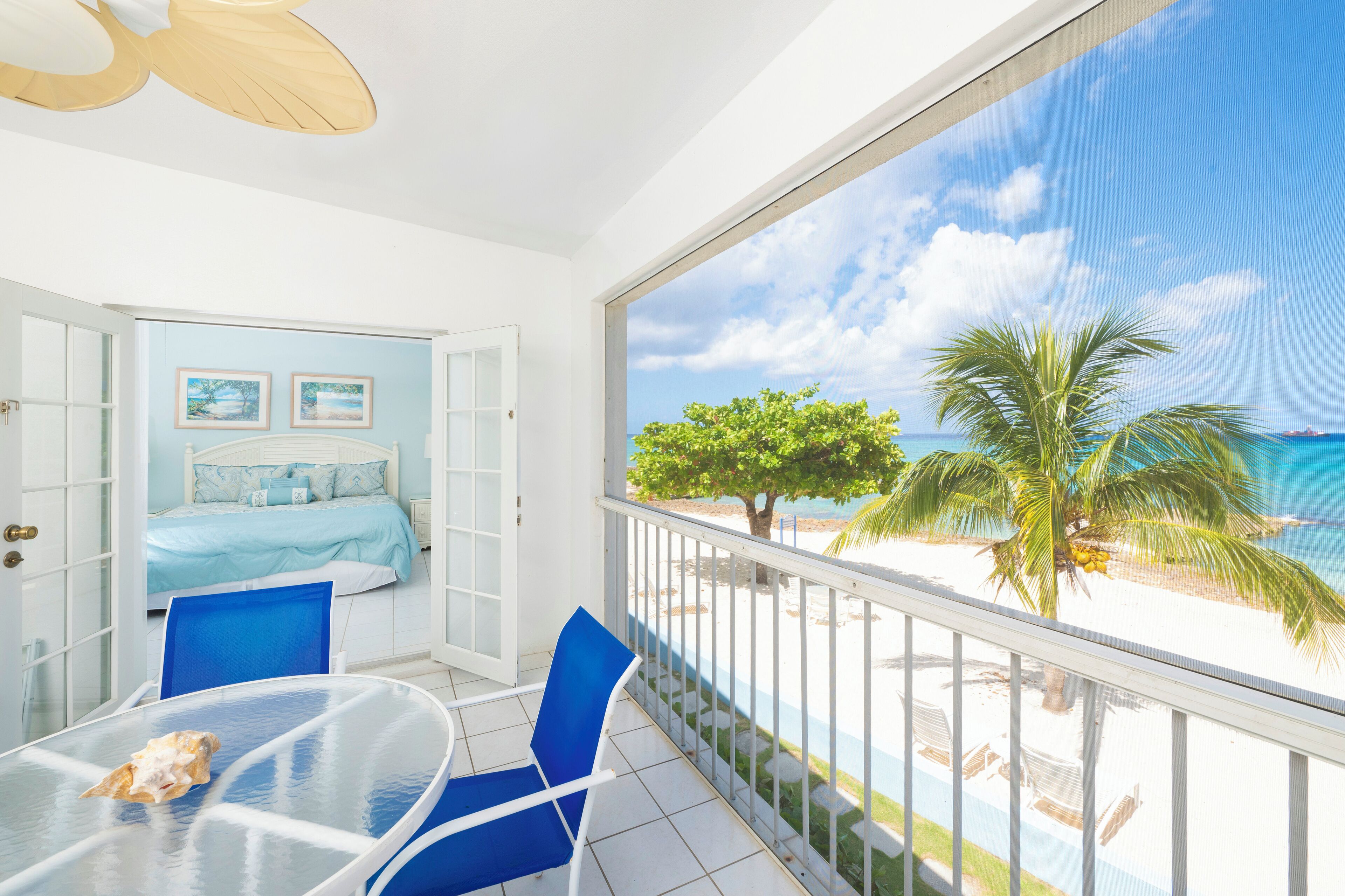 Un balcon donnant sur une plage, un lit avec une literie bleue et une table avec des chaises.