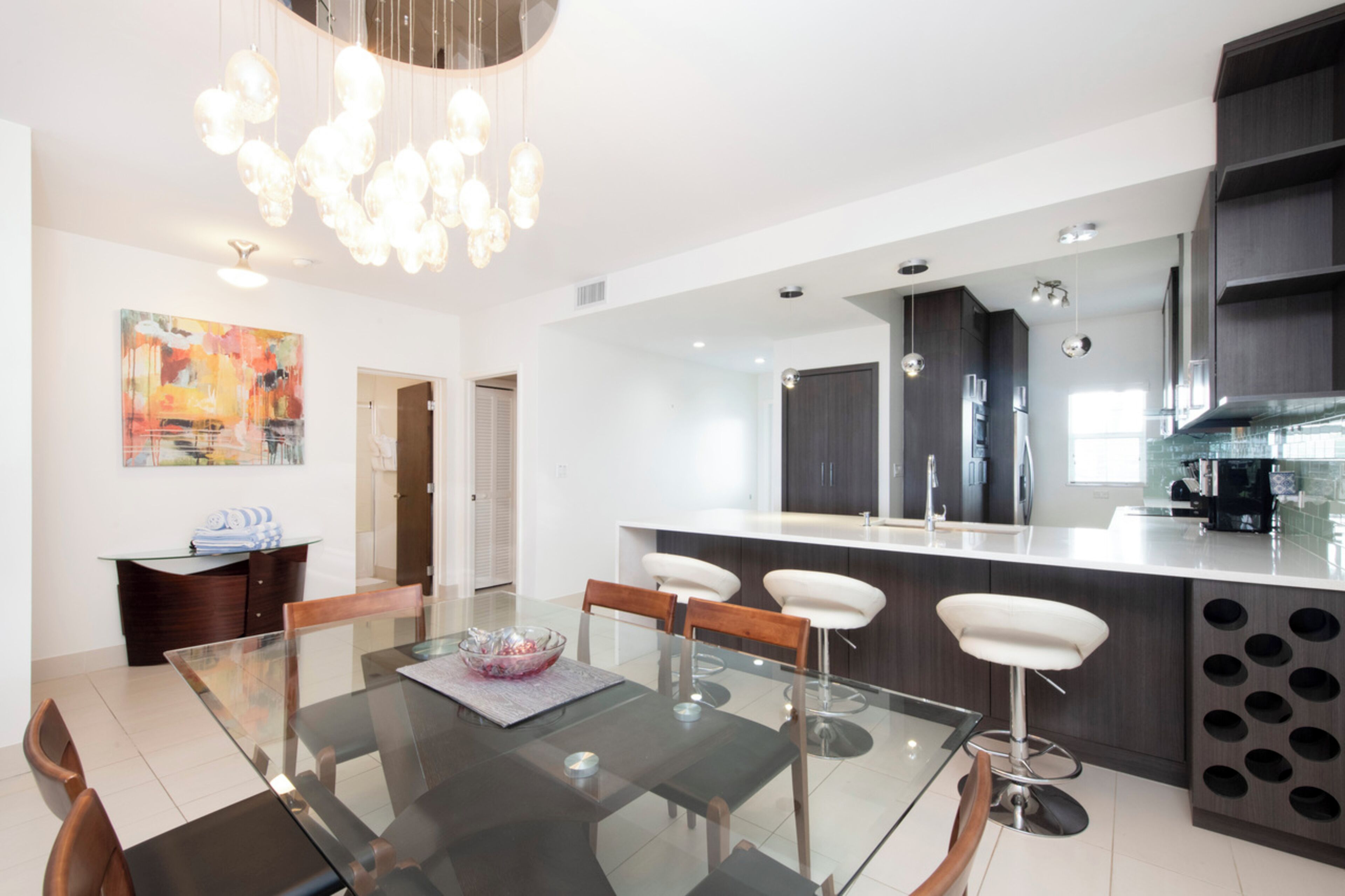 Een moderne keuken met een centraal eiland, donkere keukenkasten en een eethoek met een glazen tafel en stoelen.