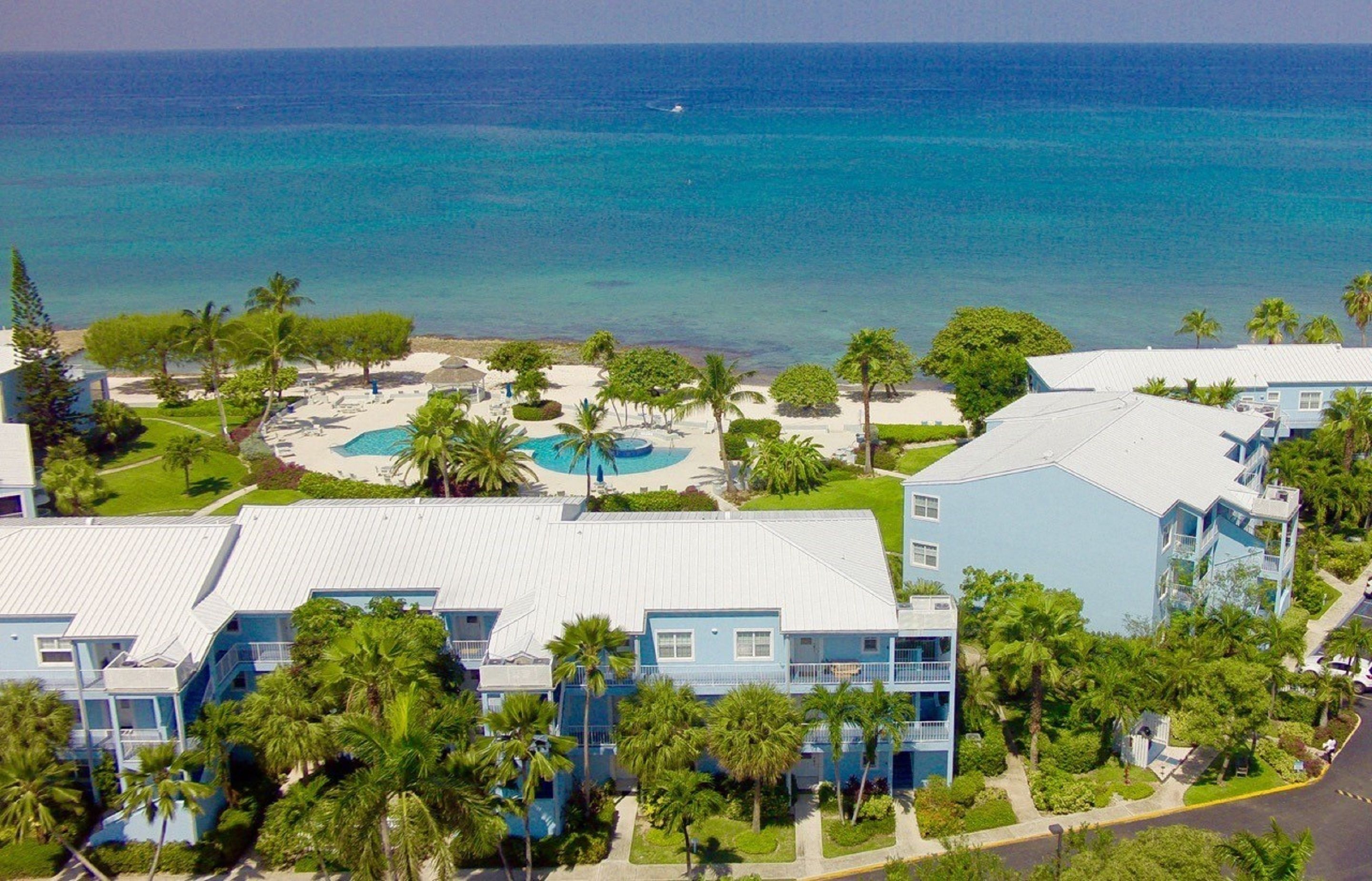 A resort with multiple blue buildings, a central pool area, and a view of the ocean.