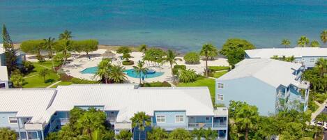 Un resort con varias edificaciones azules, un área de piscina central y vista al océano.