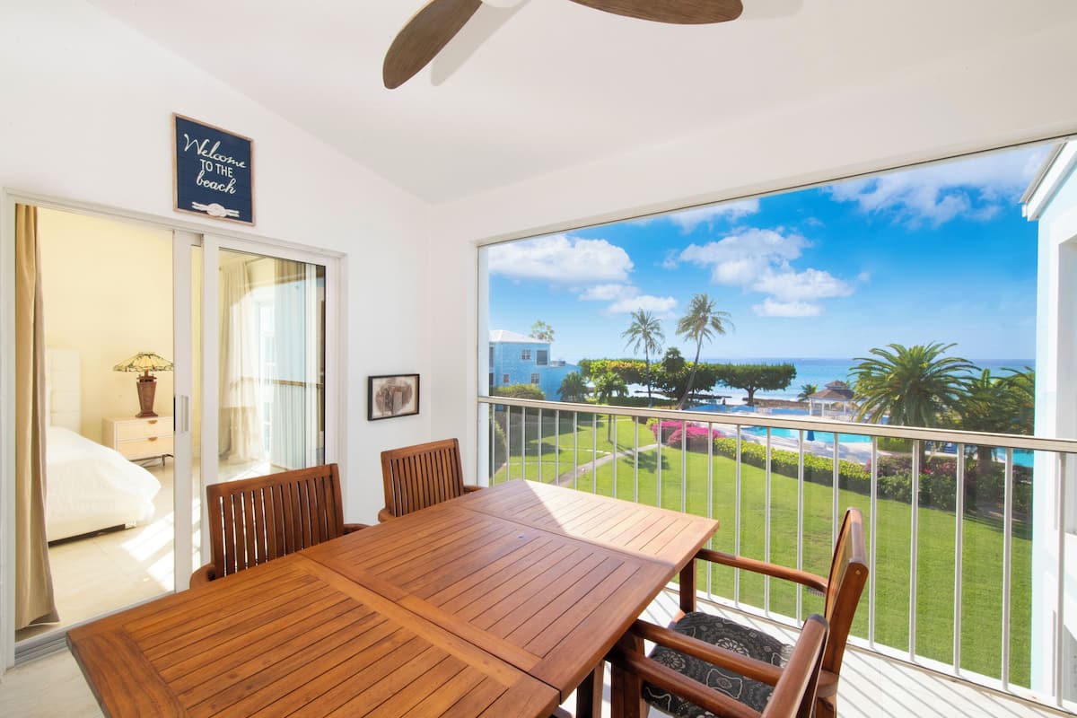 A balcony with a wooden table and chairs, a view of the ocean, and a sign that reads "Welcome to the beach."