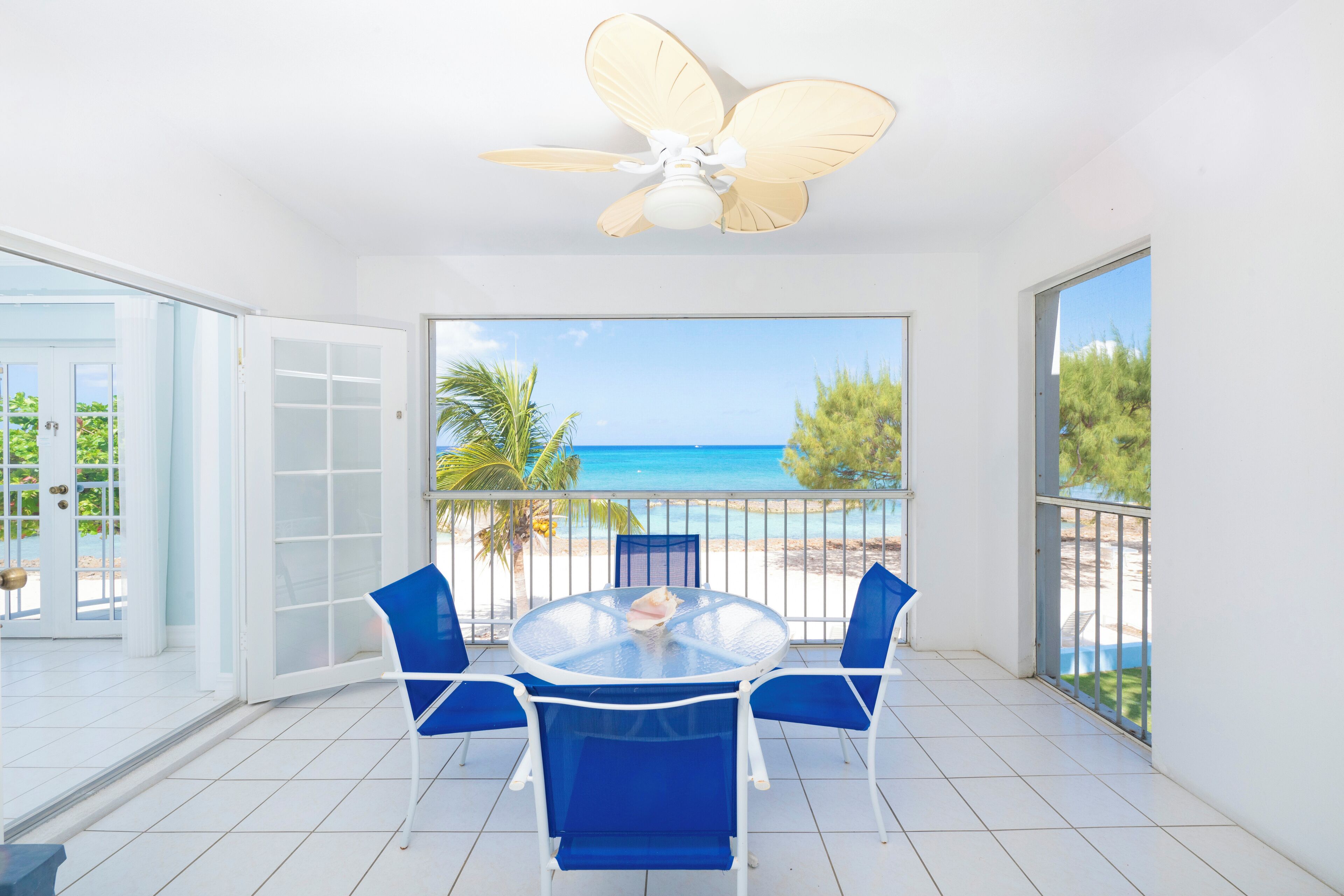 Ein Balkon mit Glastisch, blauen Stühlen und Deckenventilator.