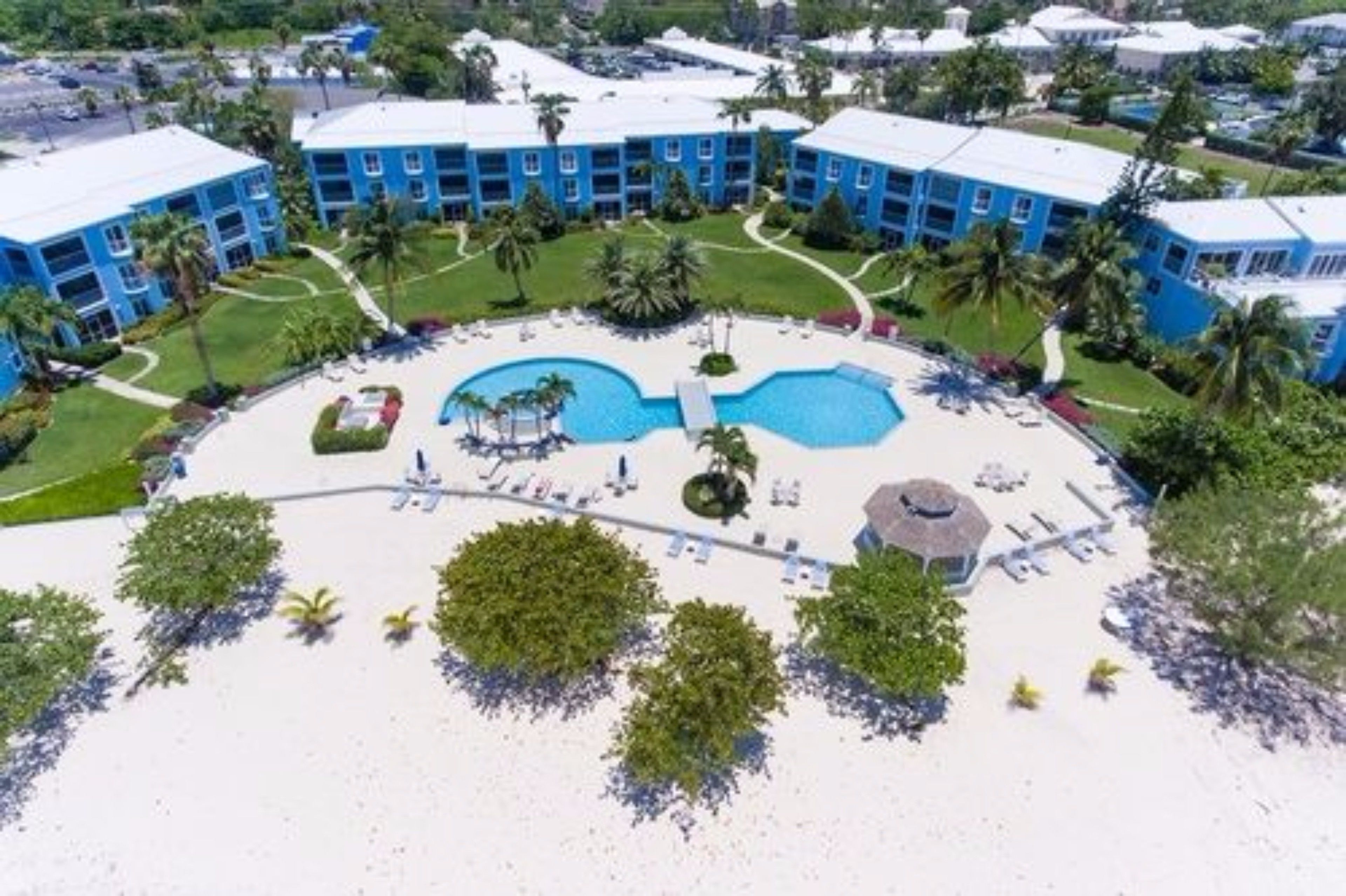 A resort with multiple blue buildings, a central pool, and surrounding greenery.