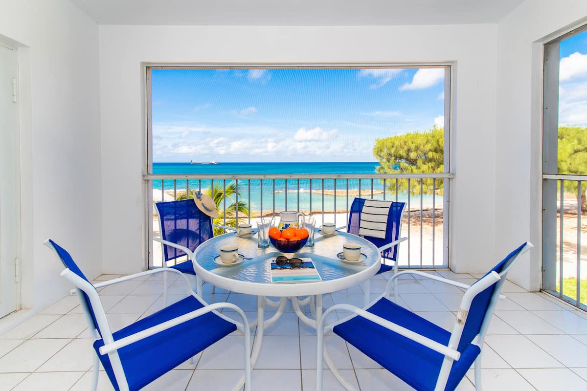 A balcony with a table, chairs, and a view of the sea.