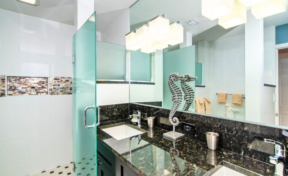 Un baño moderno con mampara de vidrio, un espejo grande, un lavamanos con encimera de mármol y un perchero para toallas.