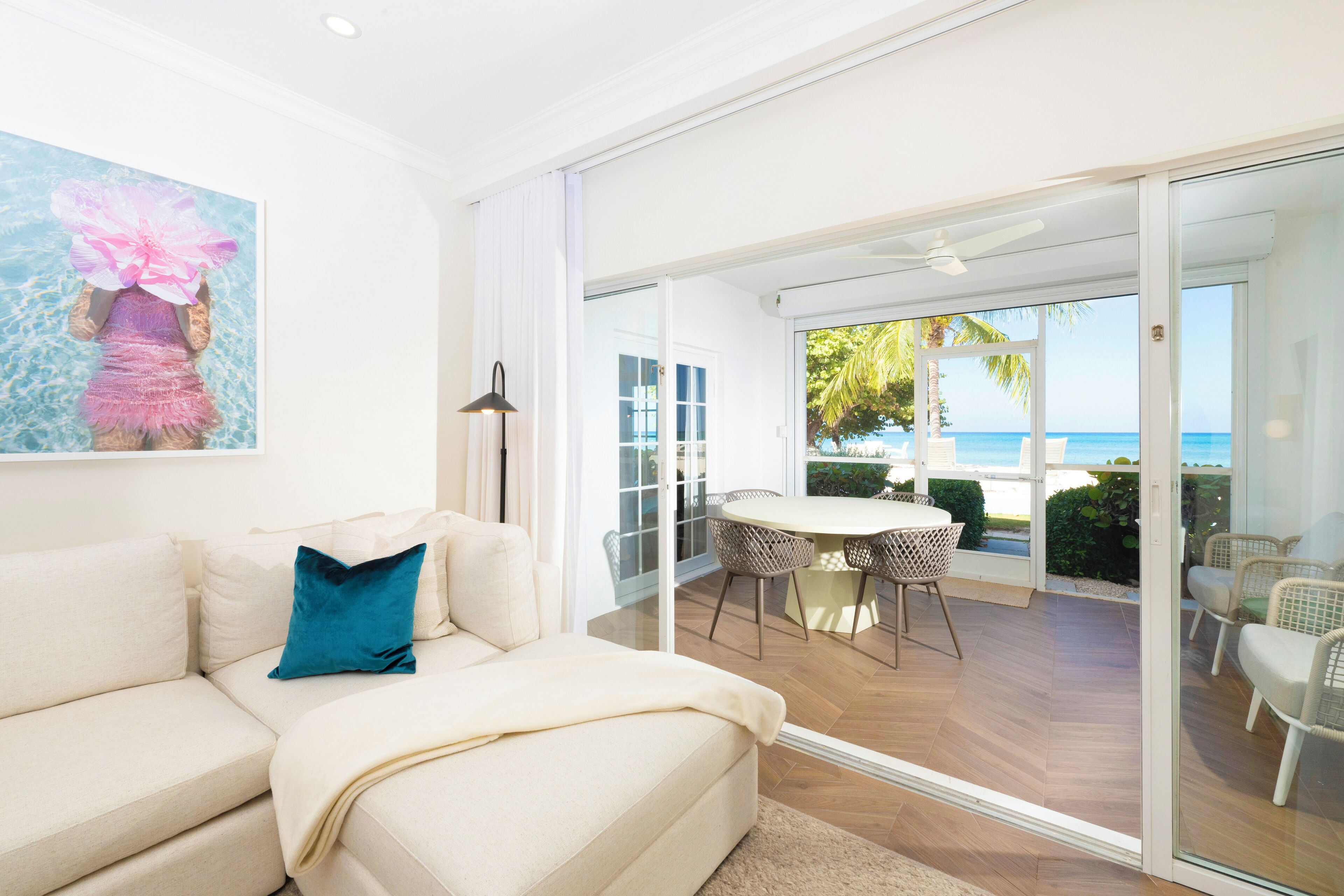 Un soggiorno moderno con un divano, un tavolo e delle sedie, che si apre su un balcone con vista sul mare tramite una porta in vetro.