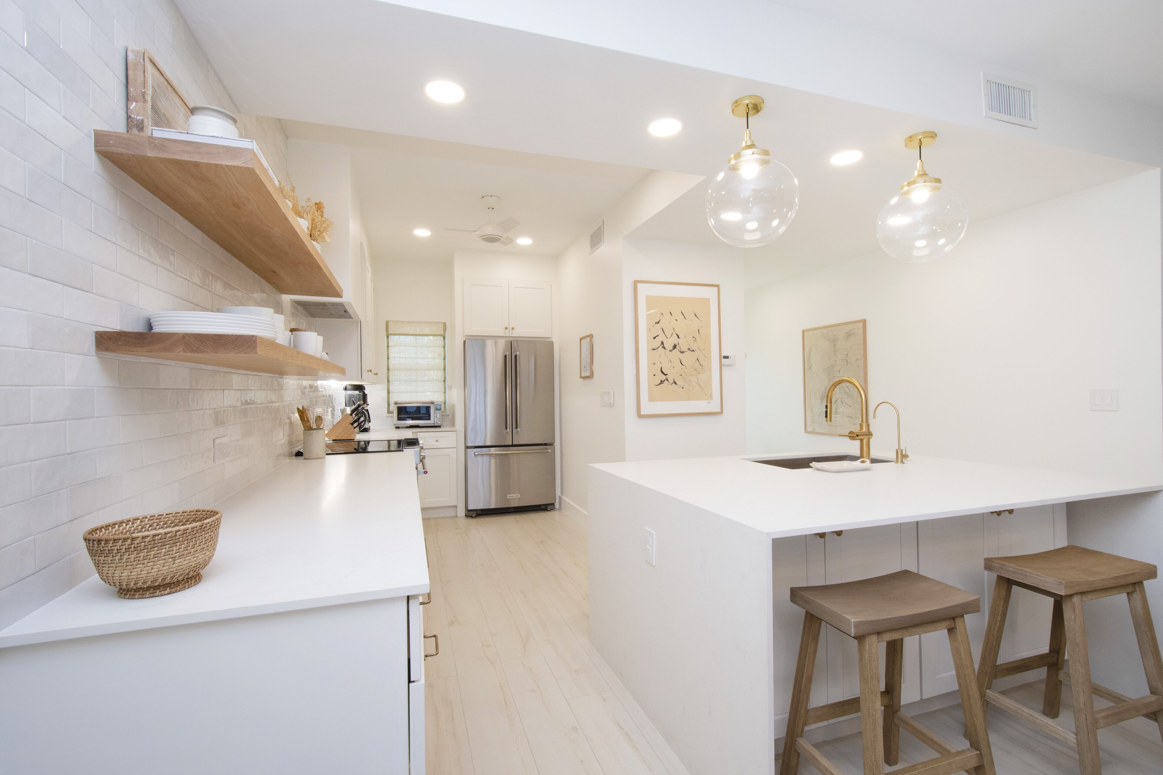 A modern kitchen with white cabinetry, a large island with stools, a refrigerator, and pendant lighting.