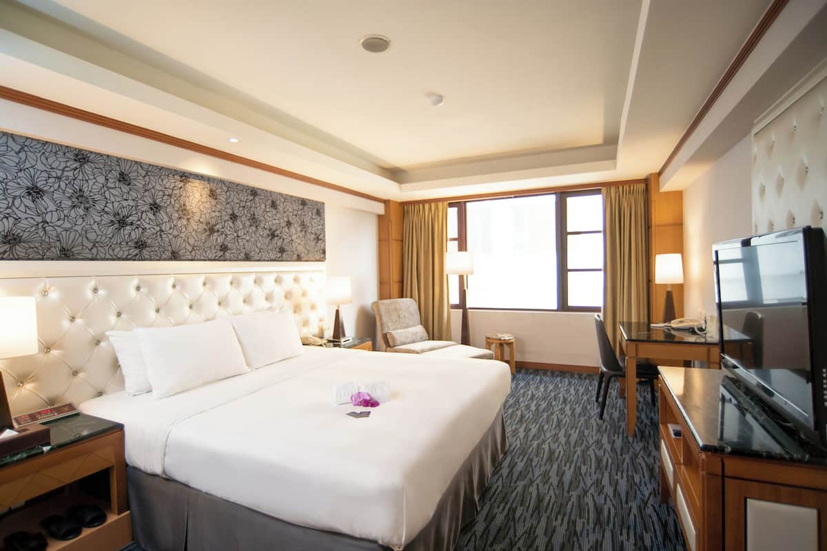 A hotel room with a large bed, a desk with a TV, a chair, and a window with curtains.