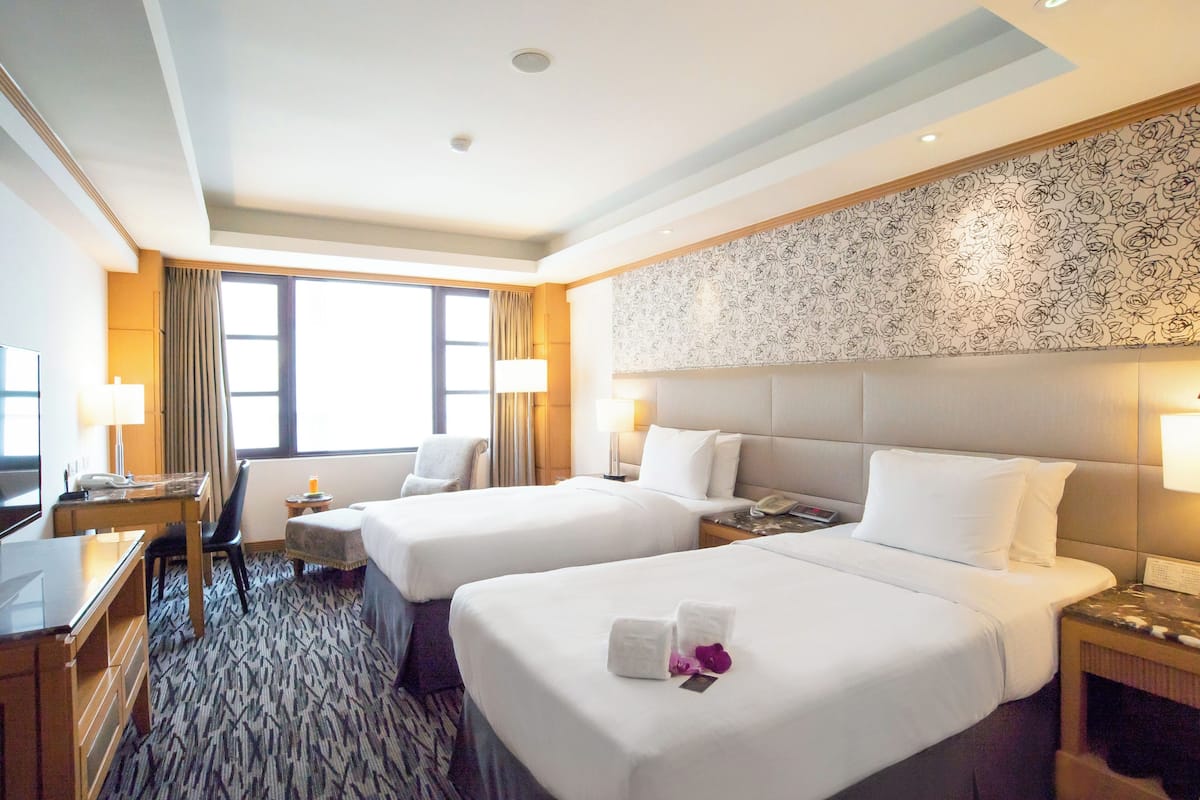 A hotel room with two beds, a desk, a chair, a TV, and a window with curtains.