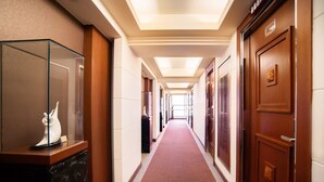 A hotel corridor with a red carpet, wooden doors, and a glass display case with a white statue. - Hotel Dion (Taichung)