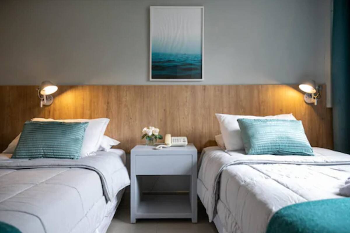A hotel room with two beds, a wooden headboard, a nightstand with a phone and flowers, and a painting above the bed.