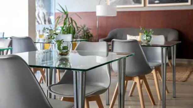 A modern dining area with glass tables and grey chairs, featuring potted plants and framed pictures on the walls. - Urbano Hotel (Montevideo)