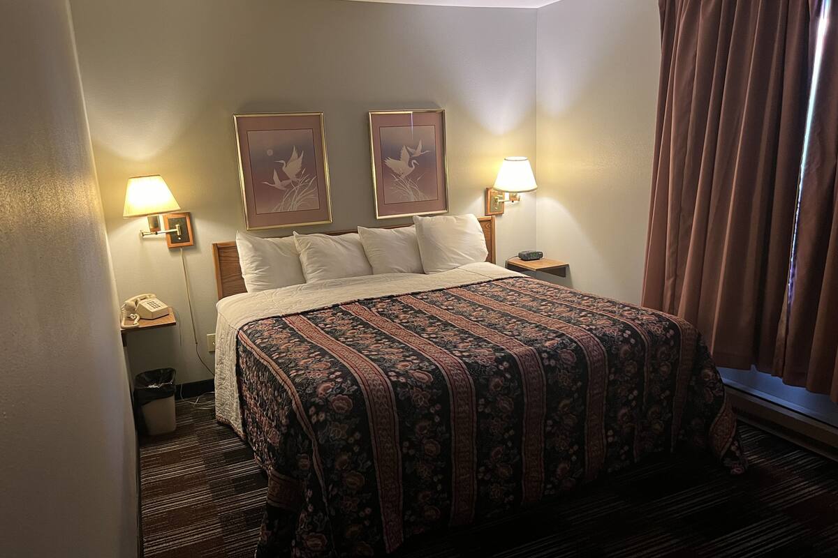 A hotel room with a large bed, two wall-mounted lamps, a telephone, and a waste bin.