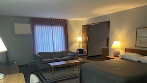 A hotel room with a bed, a sofa, a chair, a desk, and a lamp. - The Ridge Hotel Portage (Portage)