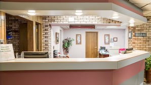 A reception desk with a brick wall backdrop, a wooden door, and a sign for Cascade Mountain Lift Tickets. - The Ridge Hotel Portage (Portage)