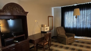 A hotel room with a flat-screen TV, a wooden desk, a chair, a microwave, and a large window with curtains. - The Ridge Hotel Portage (Portage)
