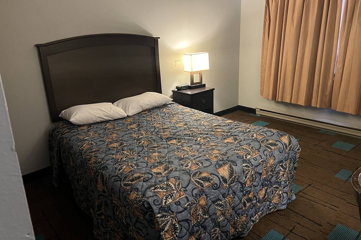 A hotel room with a bed, a nightstand with a lamp, and a window with curtains.