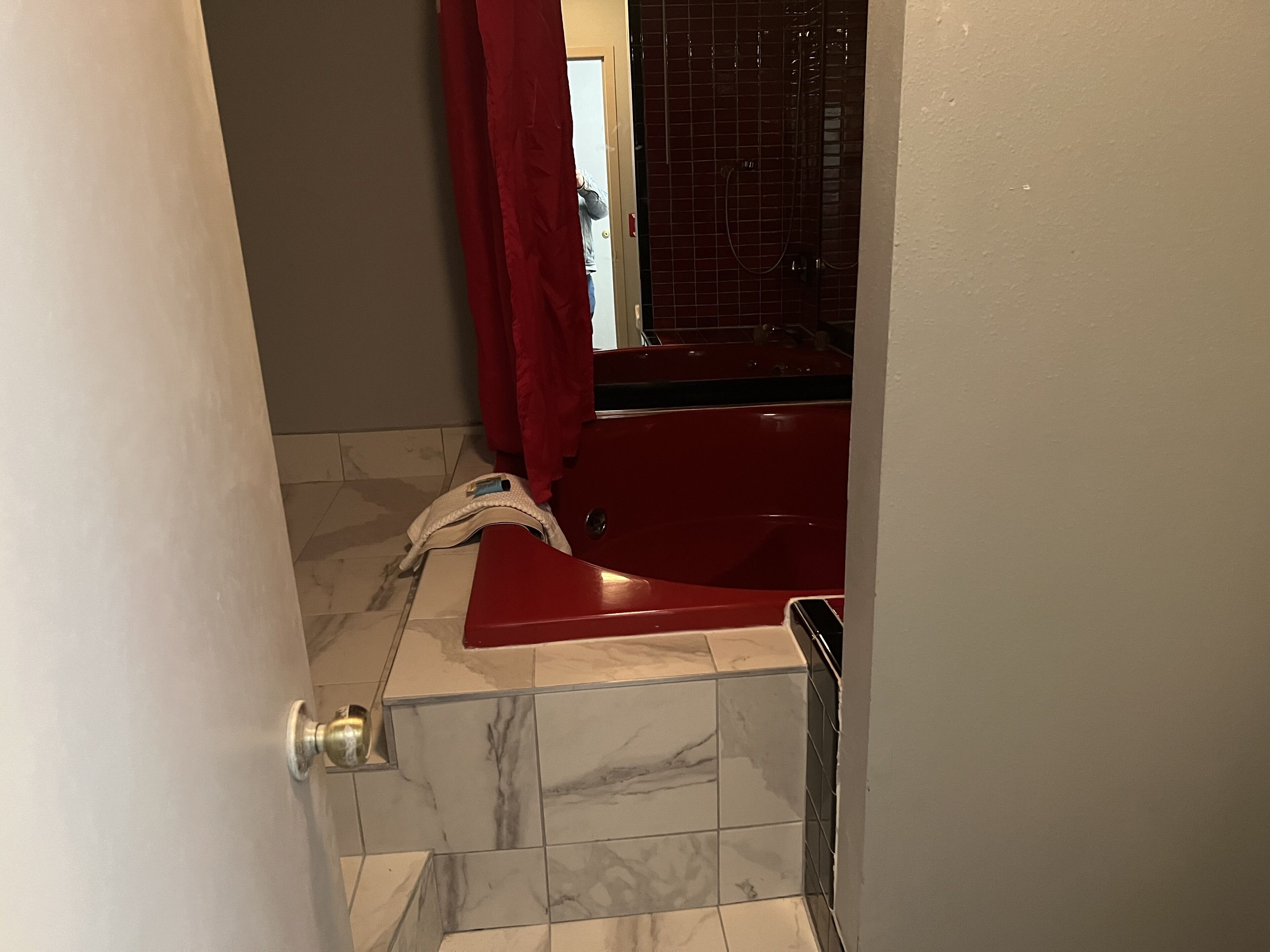 Un baño con una bañera roja, una puerta blanca y suelo de baldosas.