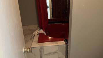 Un baño con una bañera roja, una puerta blanca y suelo de baldosas.