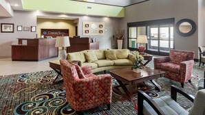 A hotel lobby with a reception desk, a sofa, two armchairs, a coffee table, and a large window.