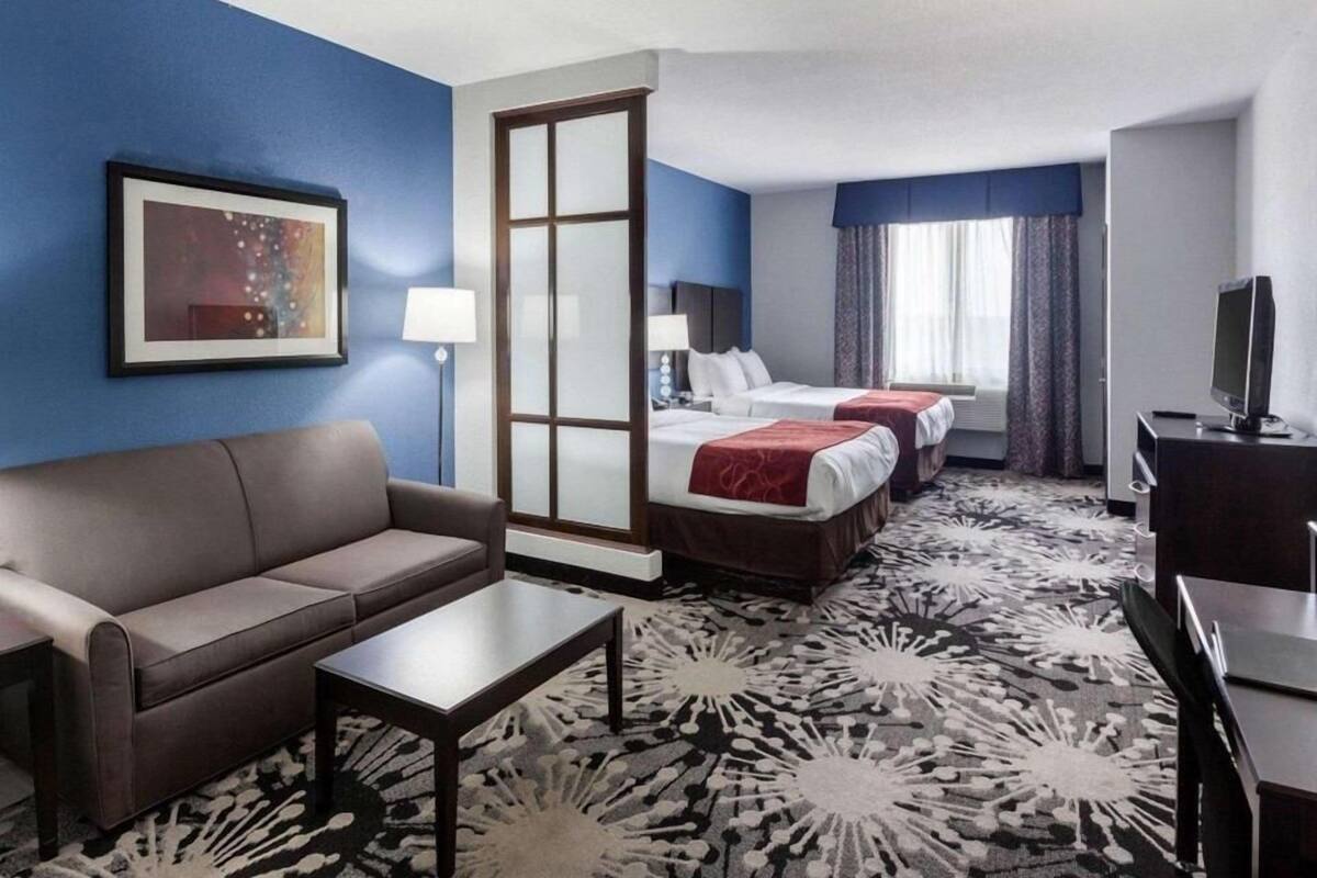 Une chambre d’hôtel avec un canapé, deux lits, un bureau, une télévision et une moquette à motifs.