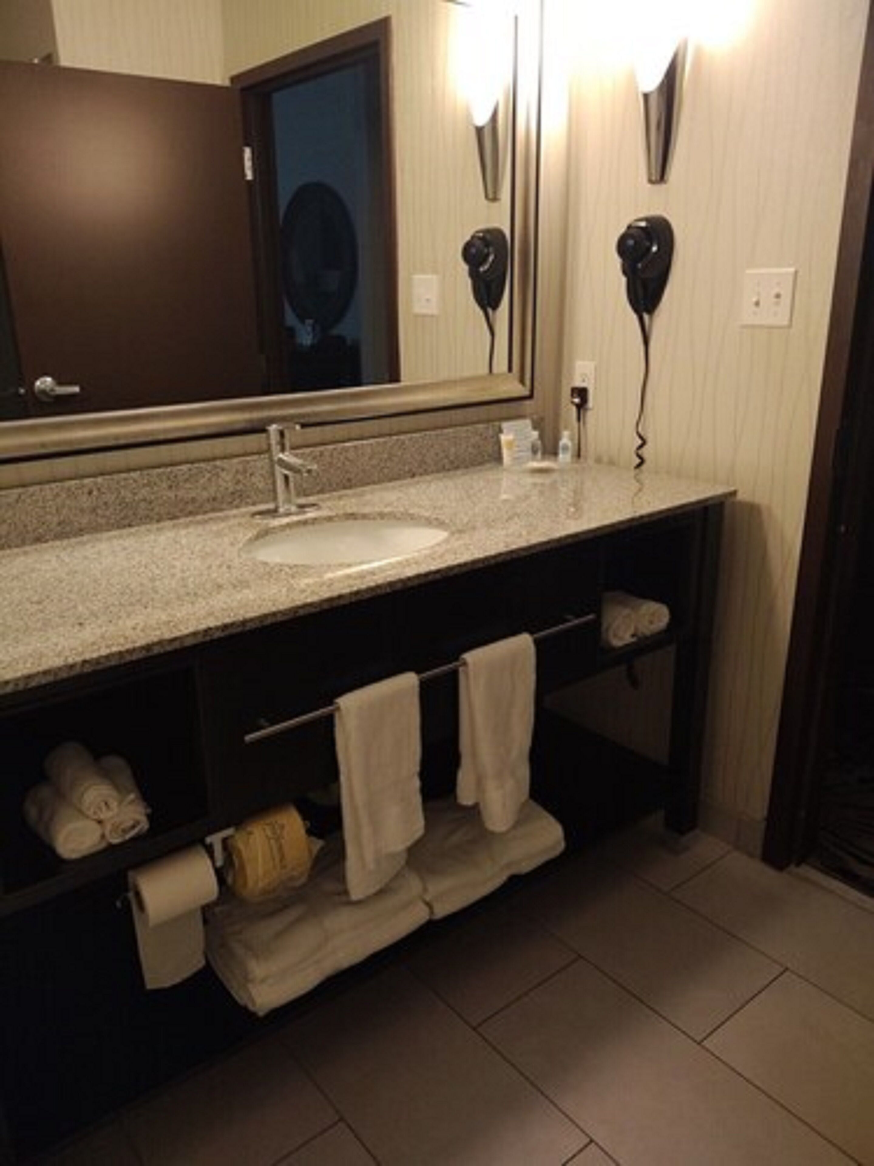 Un baño con lavamanos, espejo, toallero y secador de pelo.