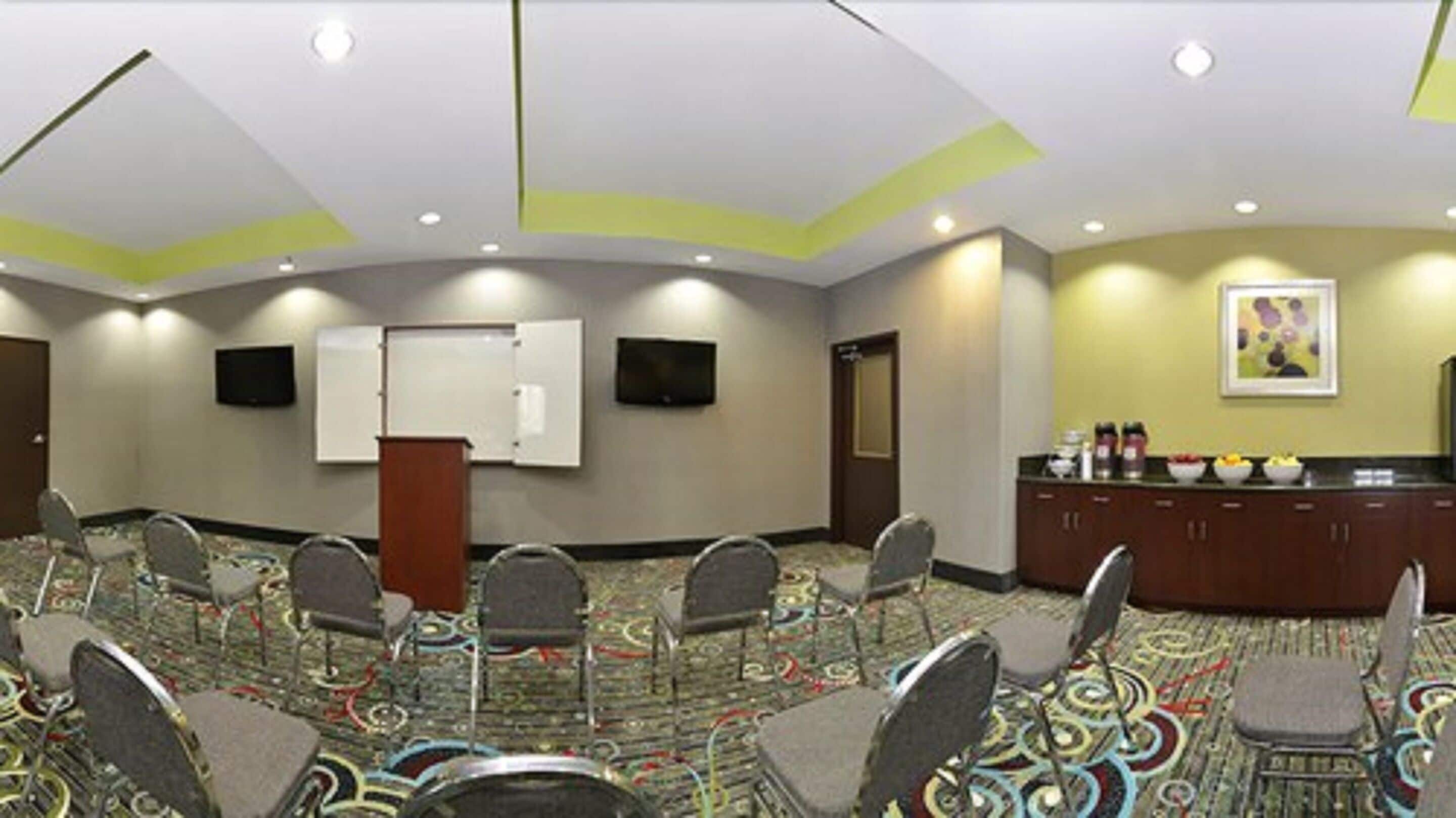 Un salón de conferencias con suelo alfombrado, un atril, una pizarra y una televisión en la pared.