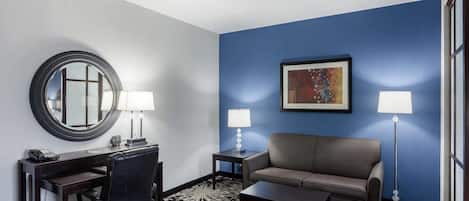 A hotel room with a desk, chair, sofa, and floor lamp.