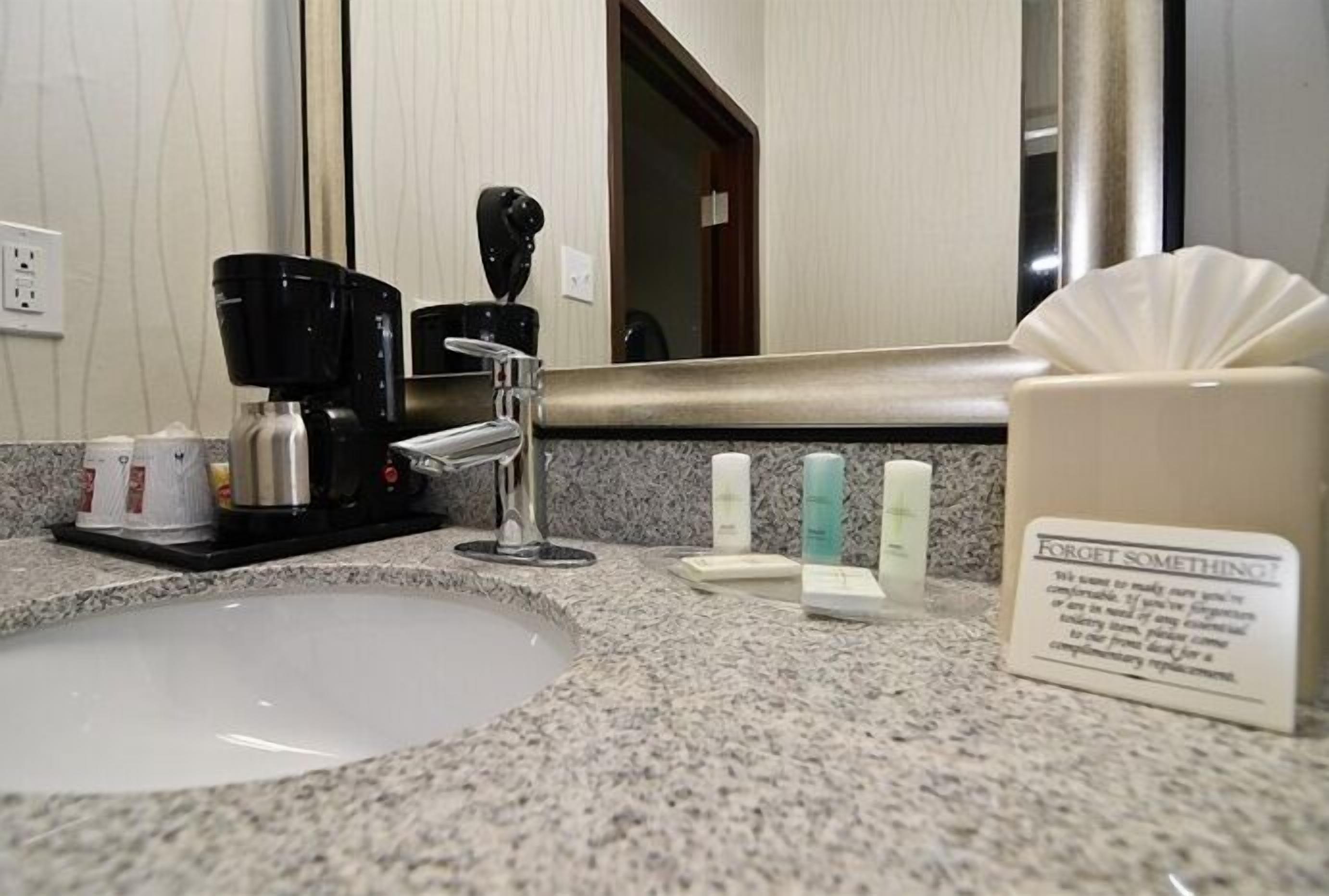 A hotel bathroom with a granite countertop, a coffee maker, toiletries, and a "Forget Something" sign.