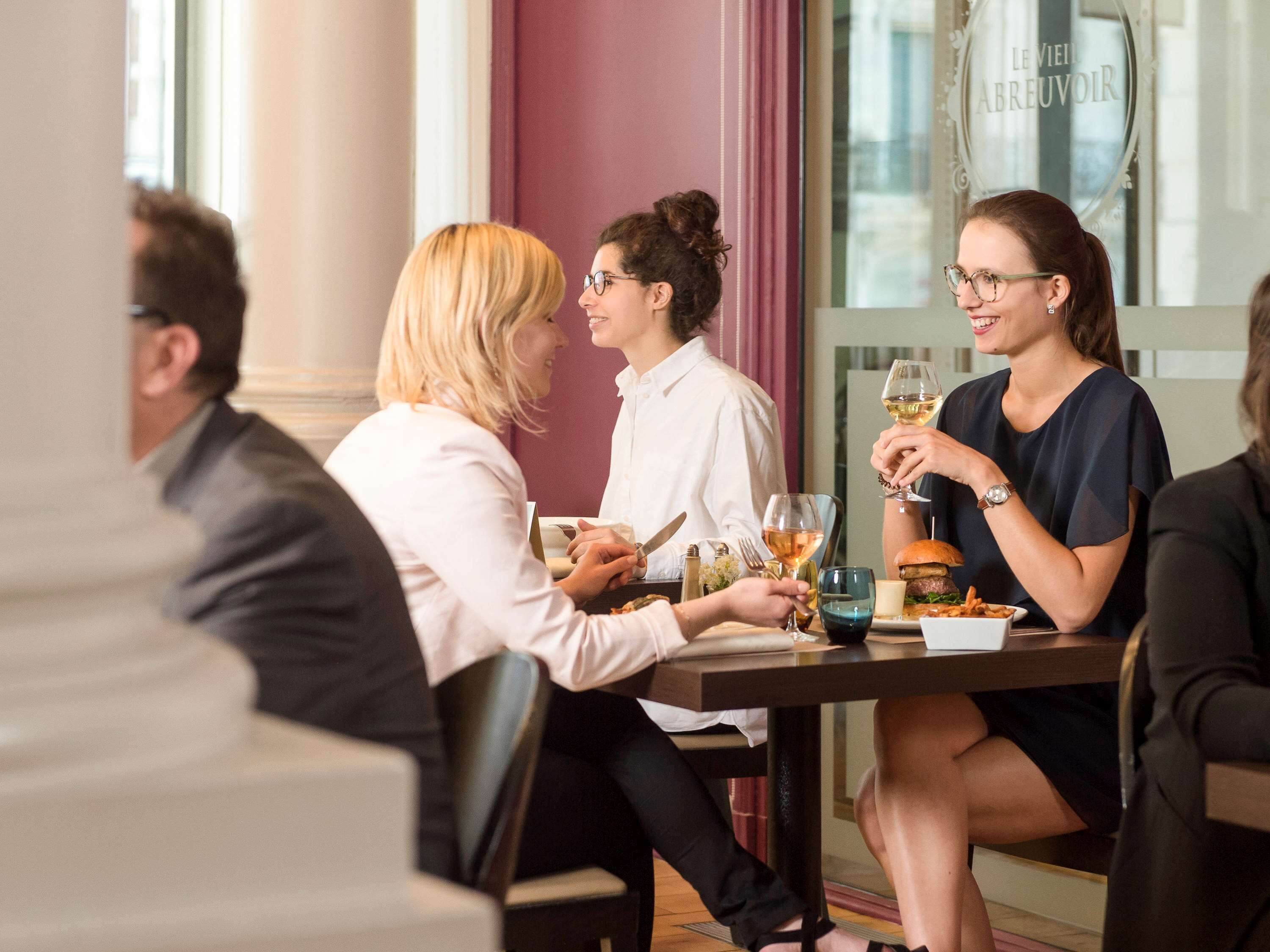 A group of people dining at a table with a view of a building outside.
