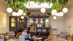 Uma área de estar moderna com mesas redondas, assentos confortáveis e um bar ao fundo.