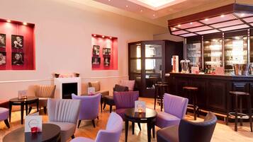 A modern lounge area with seating, a fireplace, and a bar with glassware.
