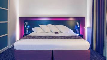 A hotel room with a large bed, a headboard with built-in lighting, a bedside table, and a window with curtains.
