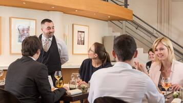 Un groupe de personnes est assis à une table dans un restaurant, avec un escalier en arrière-plan.