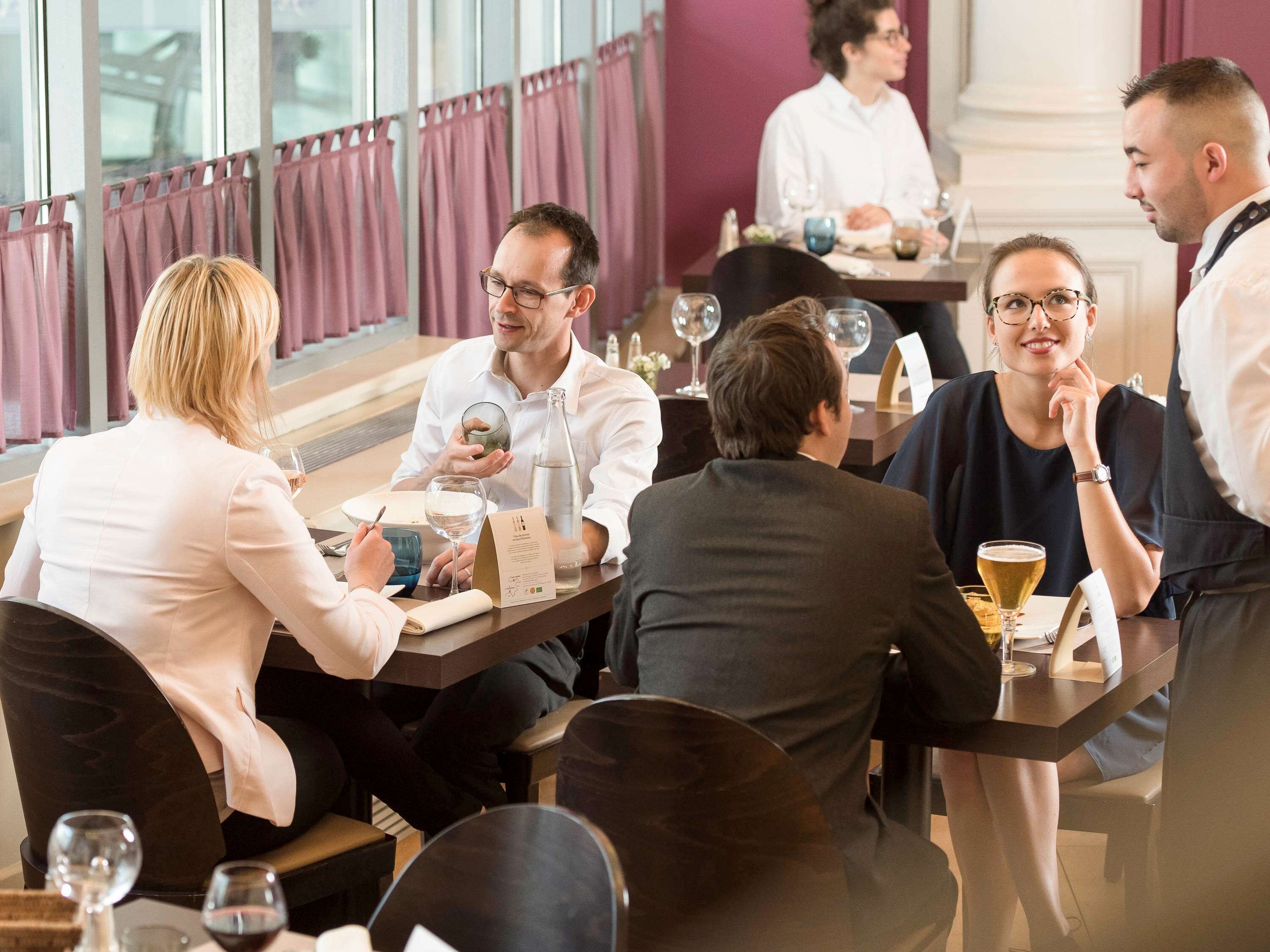 Een groep mensen zit aan een tafel in een restaurant met uitzicht op de stad door grote ramen.