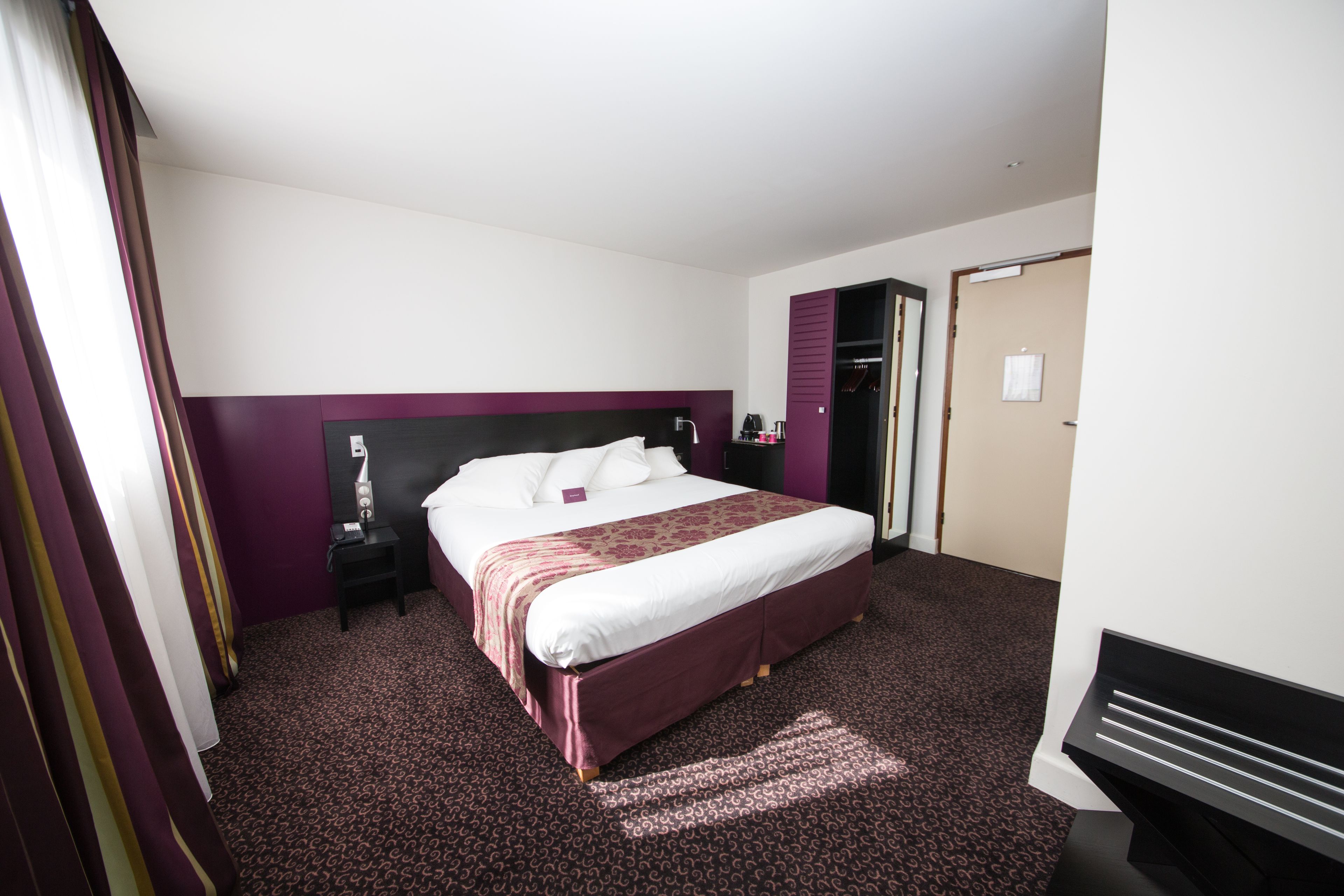 A hotel room with a large bed, a nightstand, a desk, and a wardrobe.