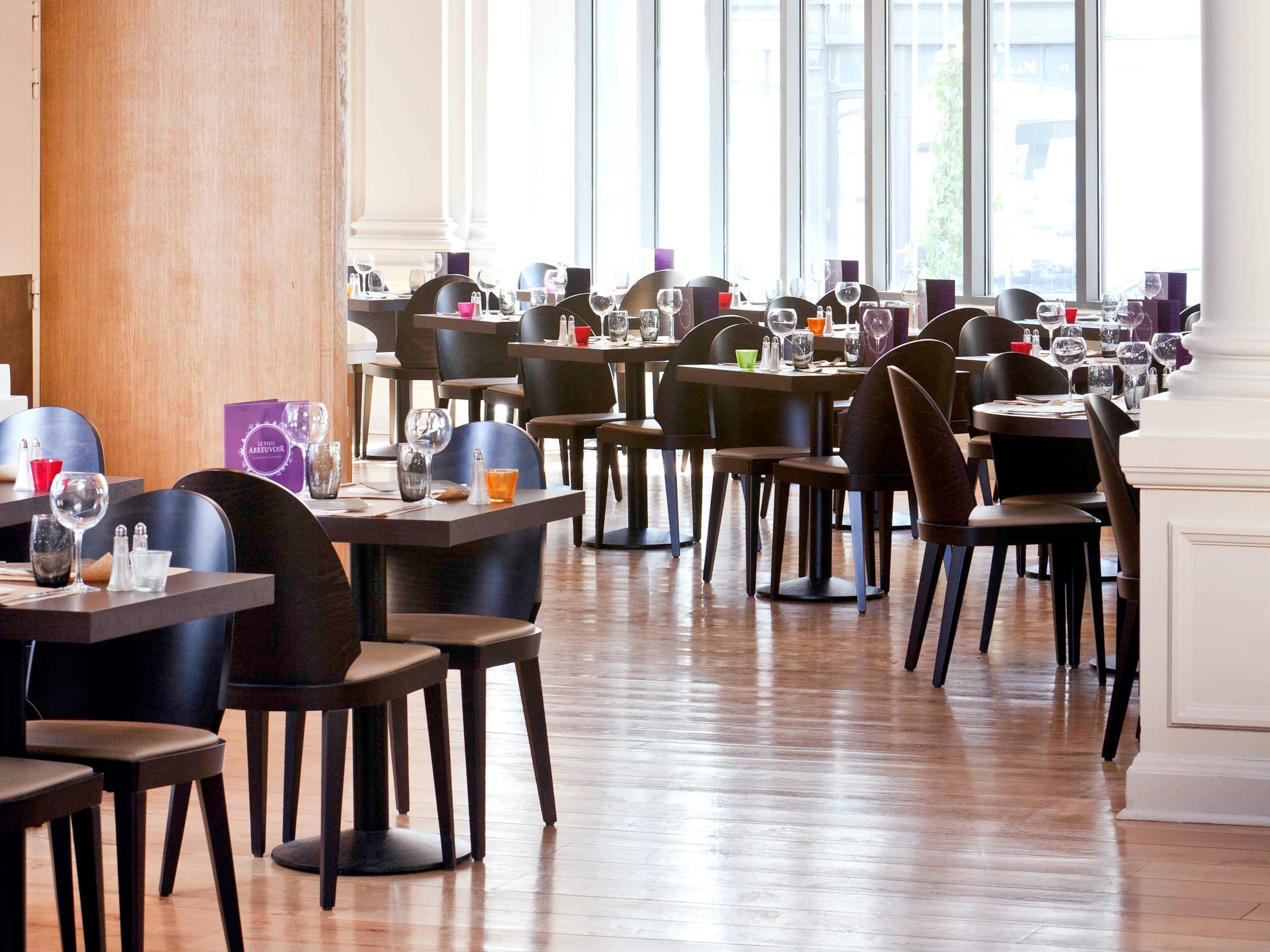 A restaurant with multiple tables and chairs, large windows, and a wooden floor.