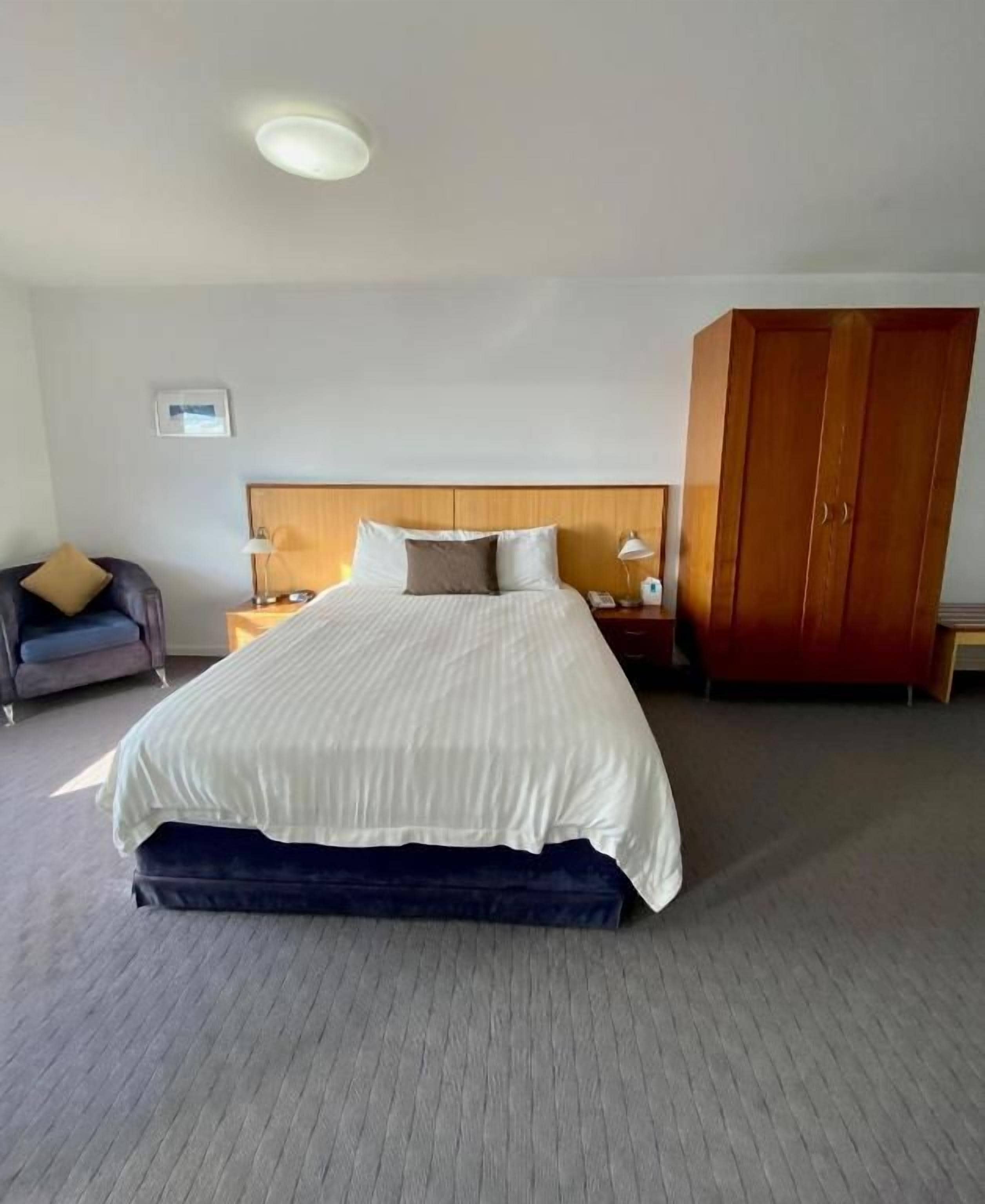 A hotel room with a large bed, a wardrobe, a nightstand, and a chair.