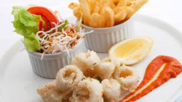 Un plato con calamares fritos, una rodaja de limón y un bol pequeño de ensalada.