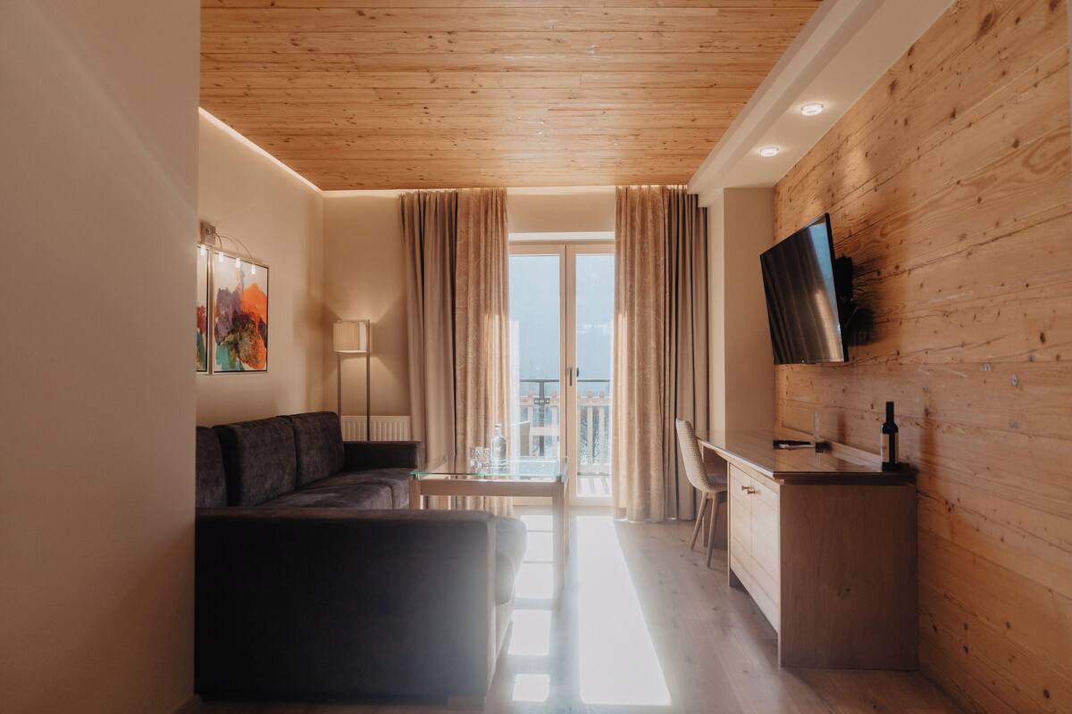 A modern living room with a sofa, a glass table, and a flat-screen TV mounted on a wooden wall.