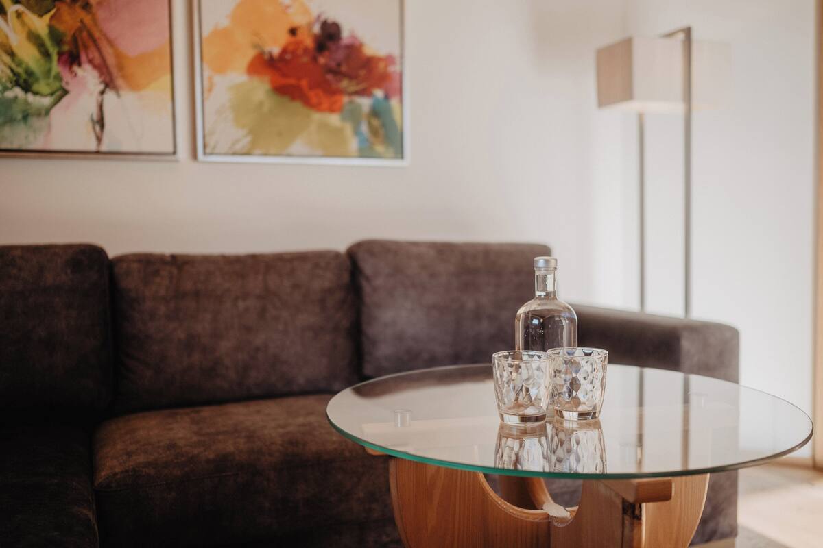 A modern living room with a glass-top coffee table, a brown sofa, and abstract paintings on the wall.