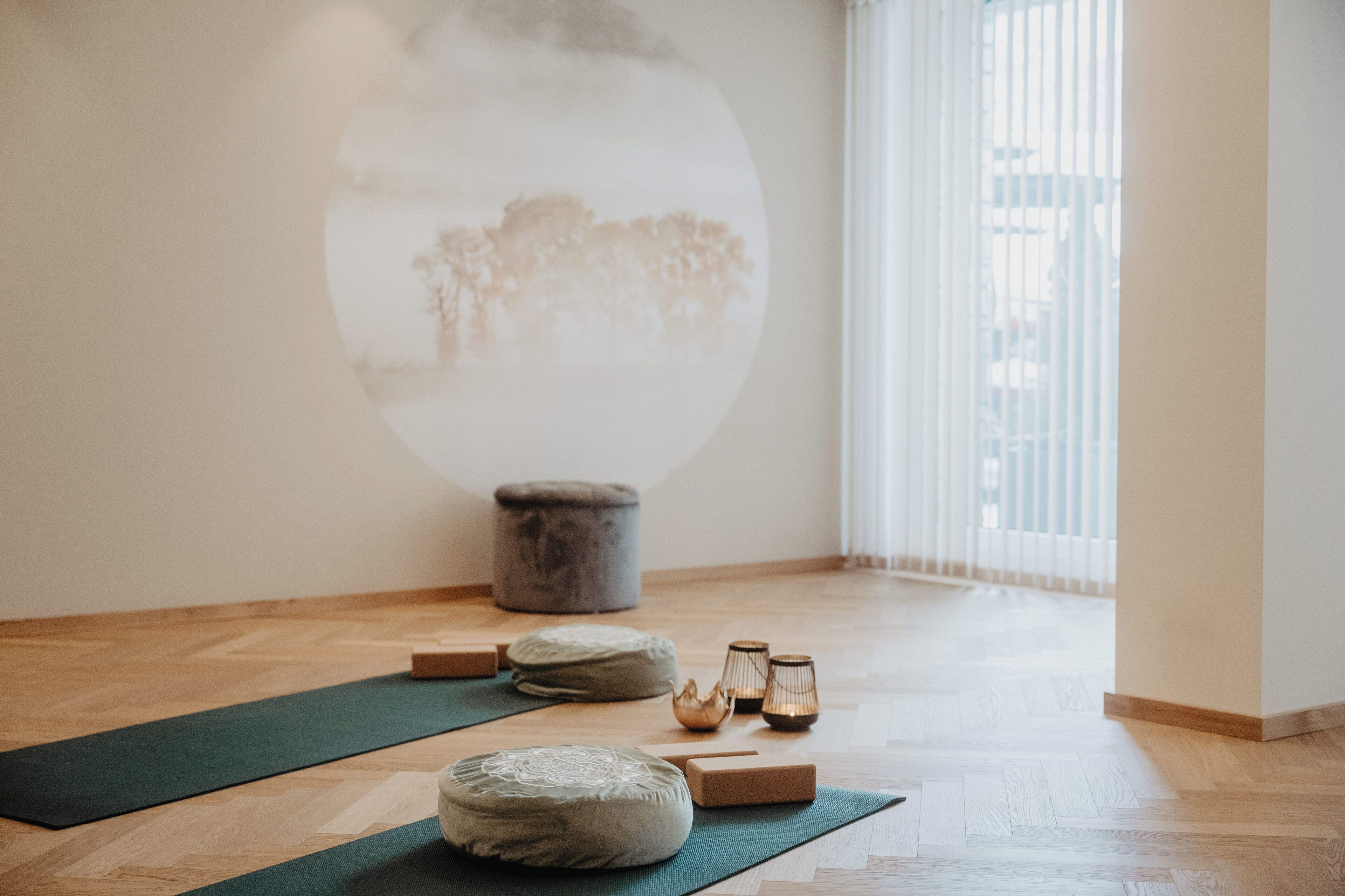 Een kamer met houten vloer, een groene yogamat, een meditatiekussen en een klein tafeltje met kaarsen.